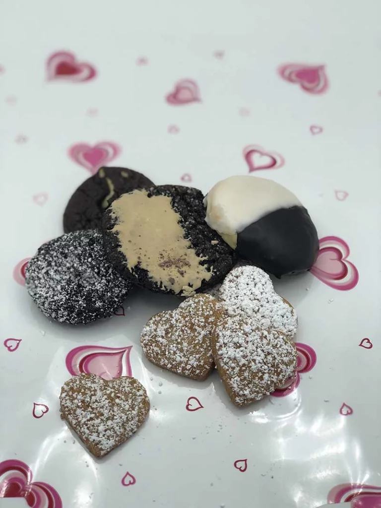 multiple heart shaped and other valentines day themed cookies on a decorative tablecloth