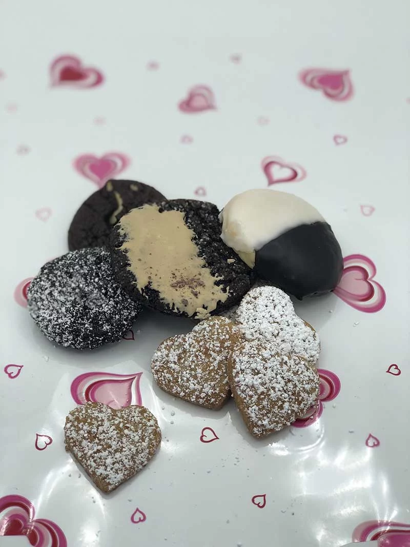 multiple heart shaped and other valentines day themed cookies on a decorative tablecloth