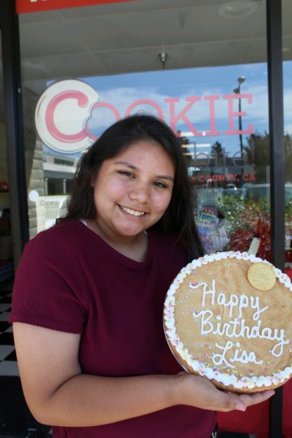 woman holding up large decorated birthday cookie cake