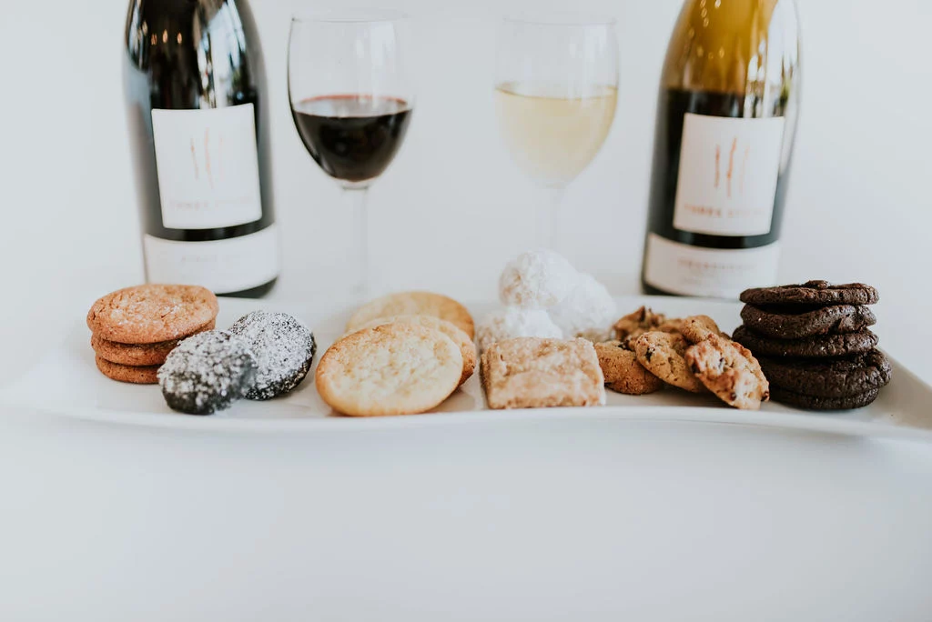 A plate of gourmet handmade cookies in front of two bottles of wine for a Valentine's Day pairing