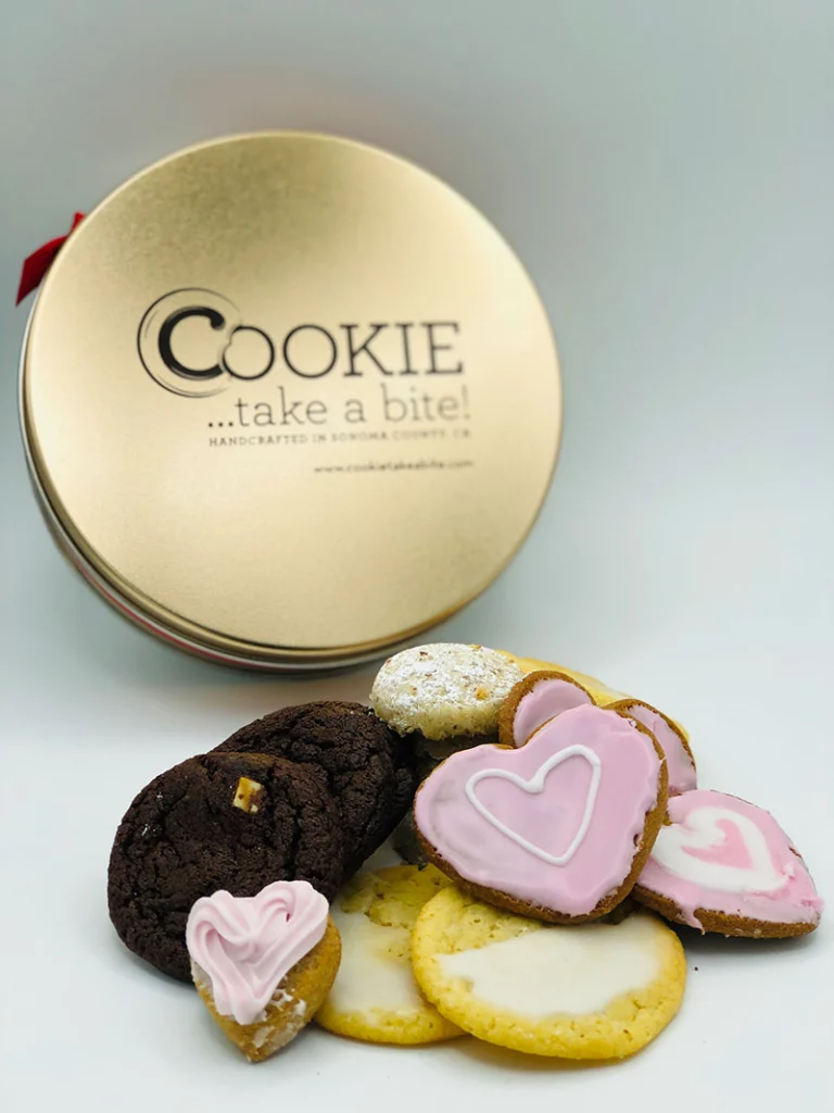 Cookie...take a bite! Deluxe Mother's Day Tin with a variety of cookies in front including pink heart-shaped cookies.