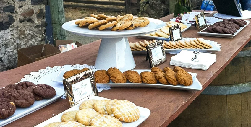 a variety of cookies displayed on a pedestal and other serving dishes with silver-framed descriptions nearby