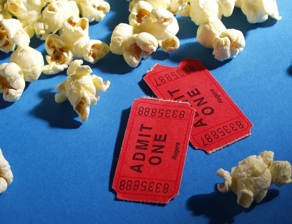 popped popcorn strewn on blue surface with two red admission tickets