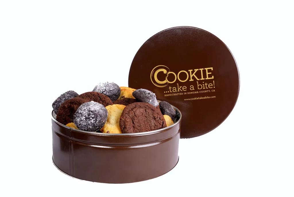 three types of cookies overflowing in brown cookie tin with lid with logo standing up behind