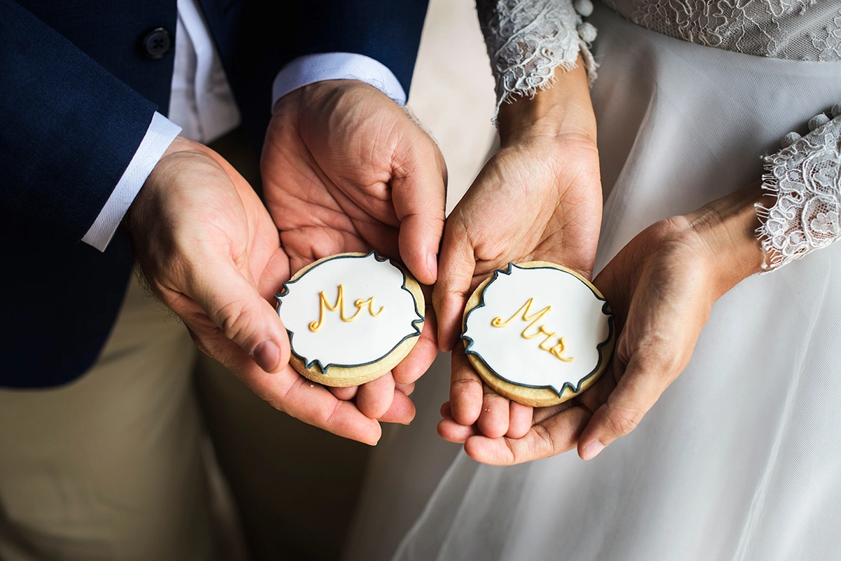 Newlywed couple in wedding dress and tuxedo, holding custom wedding cookies that read "Mr." and "Mrs."