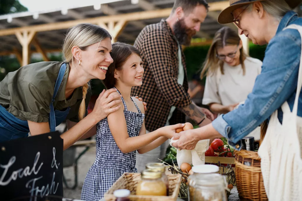 A woman and her daughter buy fresh eggs at a farmer's market to support the local economy.