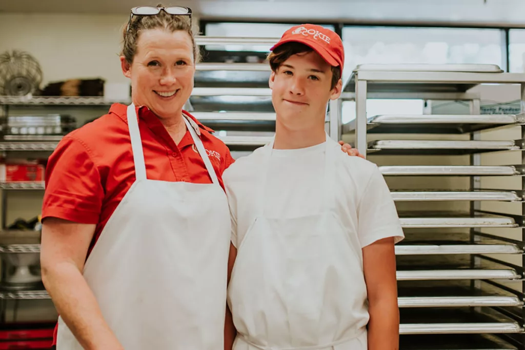 A woman and her son smiling in the kitchen of a small family owned bakery that bakes locally made cookies.