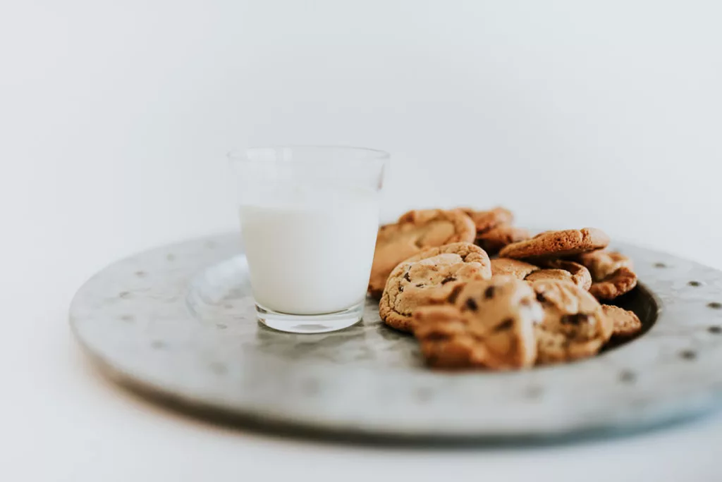 A plate of classic chocolate chip cookies against a white background, and a glass of milk.