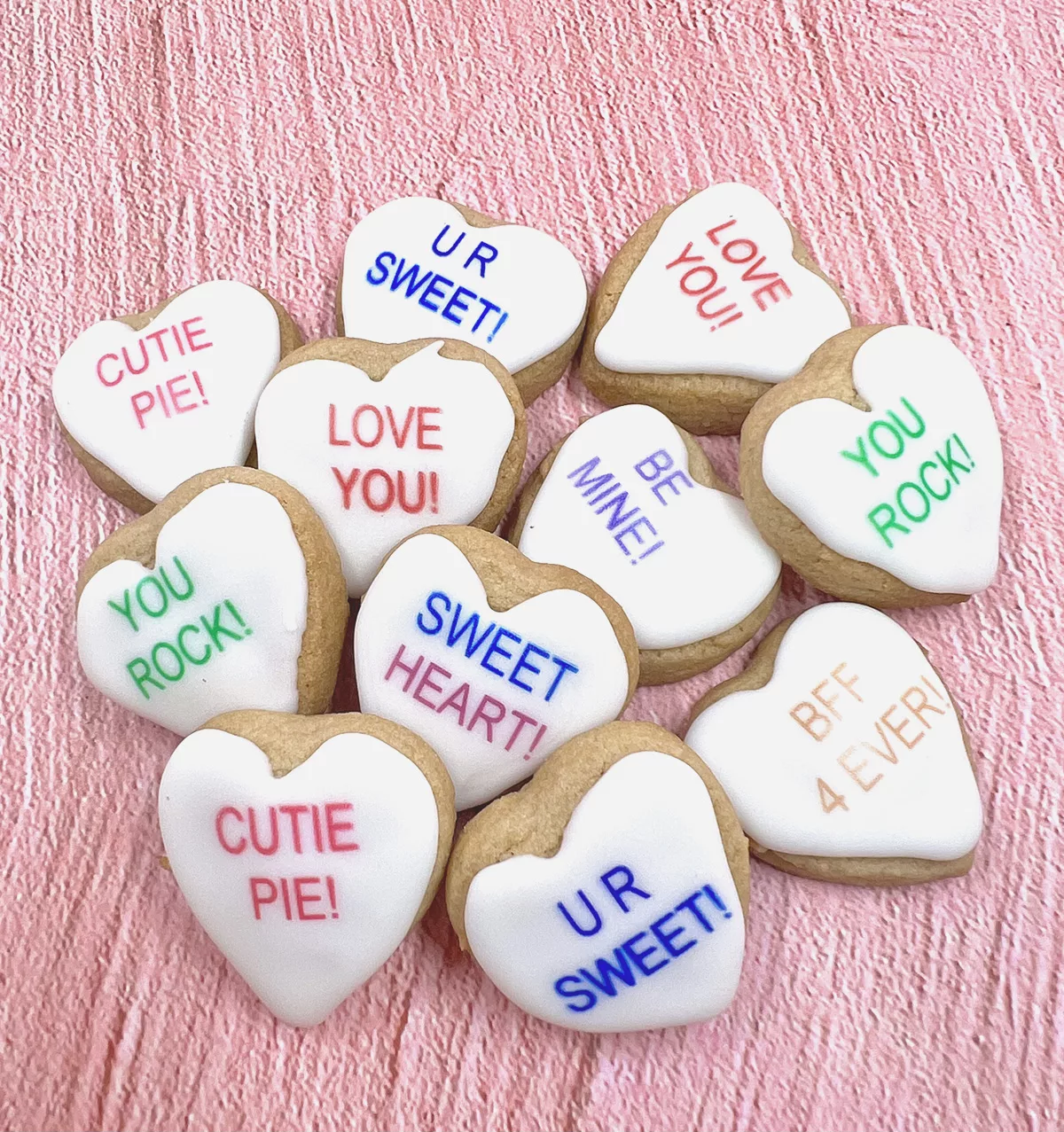 A batch of Valentine's Day conversation heart sugar cookies against a pink background.
