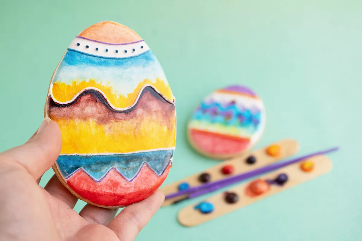 A DIY edible watercolor easter egg sugar cookie against a turquoise background