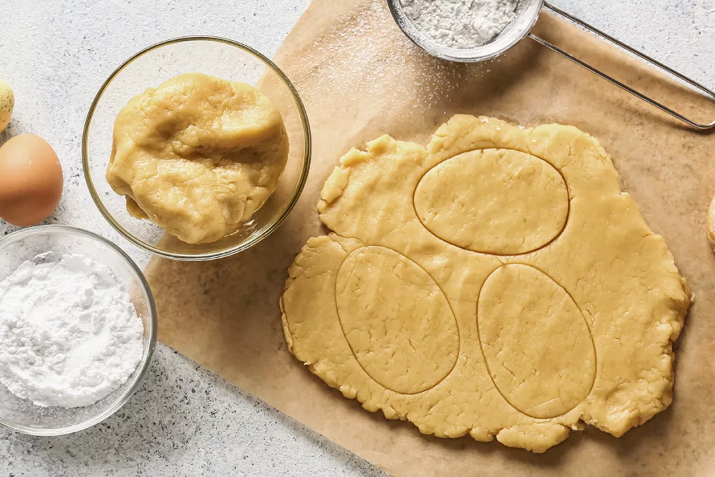 Fresh dough and ingredients for preparing DIY Easter sugar cookies on a white background