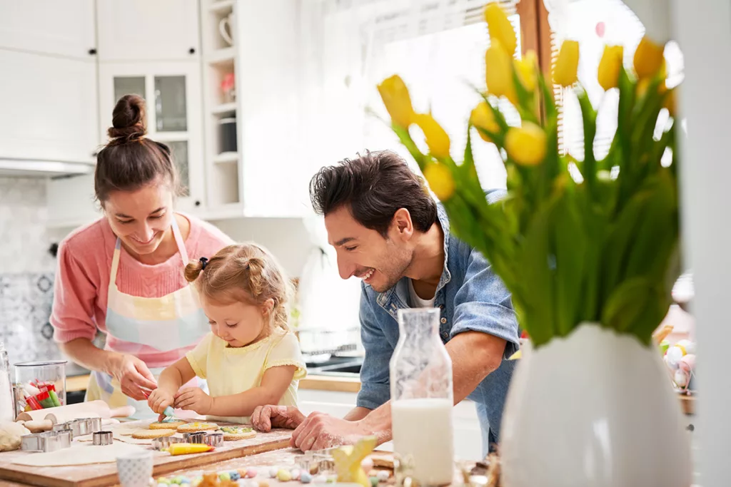 A smiling family gathers around a kitchen counter, decorating easter egg cookies.