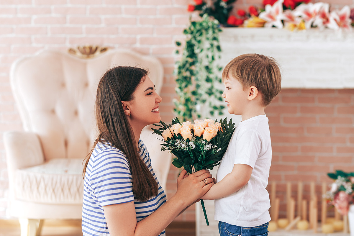 A young child hands his mom a bouquet of pink flowers as a mother's day gift.